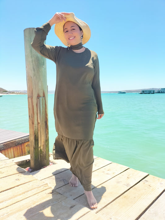 Woman in a green swimsuit standing on a wooden dock by a turquoise body of water.