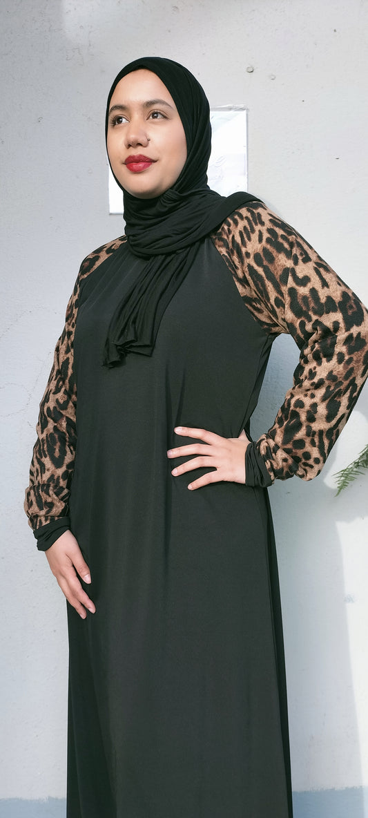 Woman wearing a black dress with leopard print sleeves against a plain background