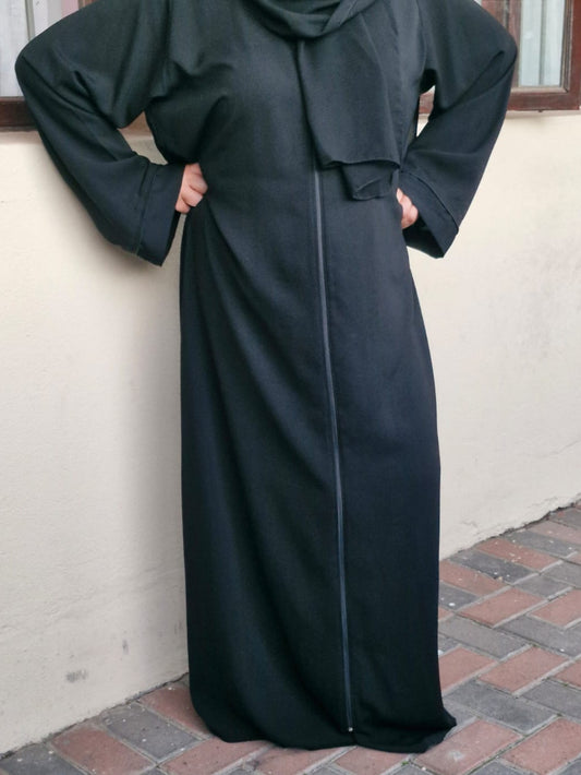 Person wearing a long black abaya standing on a pavement.