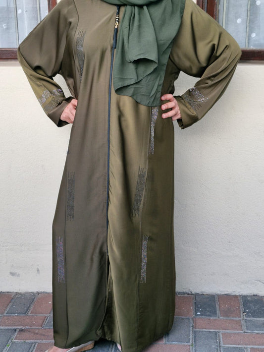 Person wearing an olive green outfit with a matching headscarf against a white wall.