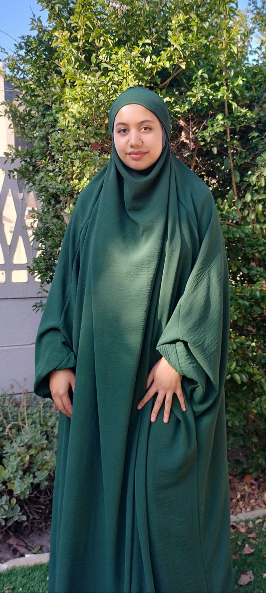Person wearing a green abaya standing outdoors with trees in the background