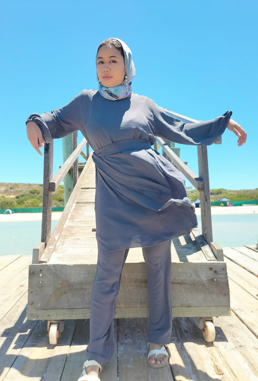 Person wearing a gray outfit on a wooden platform with a clear blue sky background