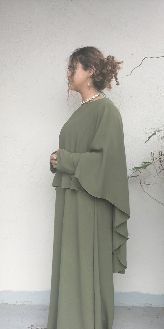 Woman wearing a long olive green dress against a white wall.