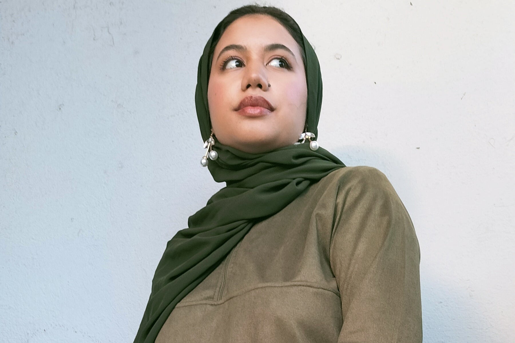 Person wearing an olive green outfit against a light blue wall