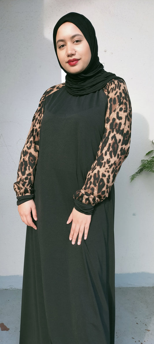 Woman wearing a black dress with leopard print sleeves against a plain background